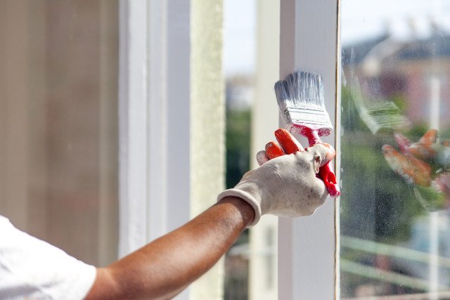 Maler streicht ein Fenster neu an.